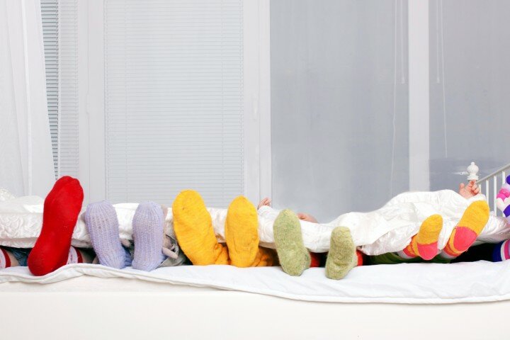 Happy family in colorful socks on white bed.